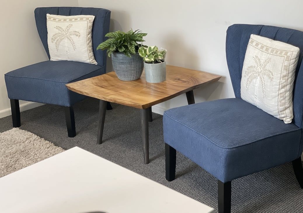 small-custom-made-coffee-table-view-2 Custom made coffee table with black legs, placed between two blue arm chairs in the client practice
